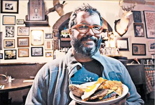  ?? MARY BERGIN/PHOTOS FOR THE CHICAGO TRIBUNE ?? Chris Breeden shows off a Yo Mama burger, whose layers include a slice of goetta, at Arnold’s Bar and Grill.