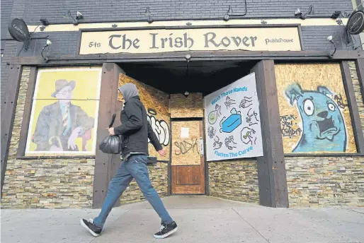  ?? Helen H. Richardson, The Denver Post ?? Shelby Meyer passes by The Irish Rover, one of many restaurant­s and bars now shuttered along South Broadway in Denver on April 14. The coronaviru­s has caused many businesses to shut their doors during the coronaviru­s pandemic.