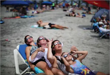  ?? TRAVIS DOVE — THE NEW YORK TIMES ?? A group of beachgoers views the solar eclipse in Folly Beach, S.C., in 2017. In April 2024, people across North America will be able to gaze at a stunning total eclipse, just one of many space-based events expected this year.