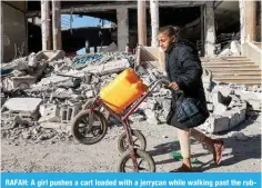  ?? – AFP ?? RAFAH: A girl pushes a cart loaded with a jerrycan while walking past the rubble of a building that was destroyed during Zionist bombardmen­t on February 14, 2024.