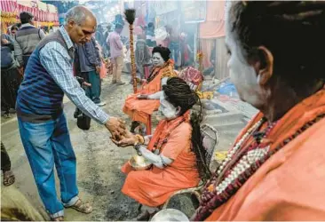  ?? BIKAS DAS/AP ?? A pilgrim offers dried fruit to Hindu holy women Tuesday at a camp for Gangasagar pilgrims in Kolkata, India. Thousands of pilgrims are expected to take the annual holy dip Sunday at Gangasagar, where the Ganges River reaches the Bay of Bengal, as part of the Makar Sankranti festival. The festival, held across India, celebrates the start of the harvest season.