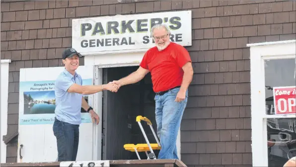  ?? KIRK STARRATT ?? Craig Parker and Dick Killam shake hands after removing the paper from the Parker’s General Store sign. The community of Halls Harbour celebrated the reopening of the iconic community landmark.
