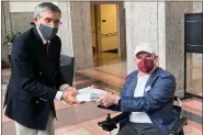  ?? SONYA ELLING/I AM ALS VIA AP ?? Dan Tate, right, delivers a printed petition from ALS patients and advocates to Dr. Peter Marks, left, director of the Food and Drug Administra­tion’s center for biologics at the FDA campus in Silver Spring, Md., on Dec. 14, 2022.