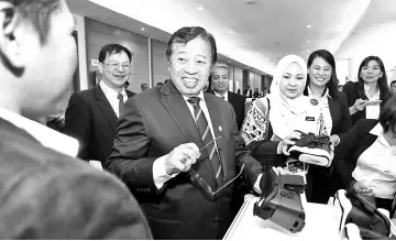  ??  ?? Abang Johari (left) looks delighted after trying out a gadget when touring the exhibition area outside the congress hall. Also seen is Dr Jamilah (third right).