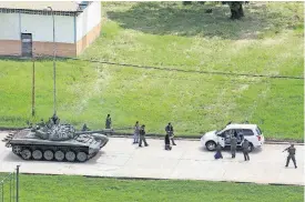  ?? [AP PHOTO] ?? Soldiers stop a vehicle whose passengers kneel on the ground outside the car while being detained Sunday on the Paramacay military base in Valencia, Venezuela.