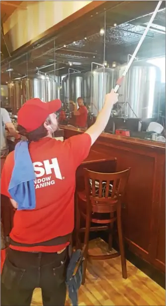  ?? BILL RETTEW JR. – DIGITAL FIRST MEDIA ?? An employee at Iron Hill Brewery cleans one of the new large windows that will allow customers to check out the area where the eatery’s signature craft beers are brewed.