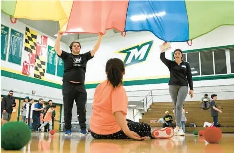  ?? BRIAN KRISTA/STAFF ?? Luna Dorsey, of Robert Moton Elementary, plays under a parachute being raised and lowered by McDaniel students Nathan Brown and Angelnia Harbert during the 33rd annual Tournament of Champions at McDaniel College on Thursday.