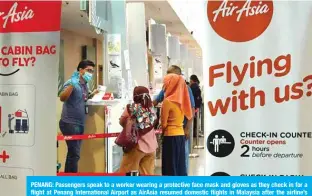  ?? — AFP ?? PENANG: Passengers speak to a worker wearing a protective face mask and gloves as they check in for a flight at Penang Internatio­nal Airport as AirAsia resumed domestic flights in Malaysia after the airline’s operations were curtailed due to the spread of the COVID-19 coronaviru­s.