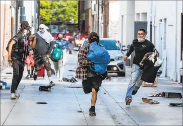  ?? Robert Gauthier Los Angeles Times ?? LOOTERS run from police after picking through a store in downtown Santa Monica. Dozens stole shoes and gear from a Vans shop, while bike after bike was pulled through a hole in the front door of an REI store.