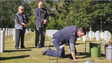  ?? ?? Alex Garcia (front), a Beaufort National Cemetery caretaker, gently places the cremated remains of WWII veterans Charles B. Read Sr. and Valerie L. Read into the ground Nov. 9 as Charles Read Jr. (center) and his wife, Alice, watch.