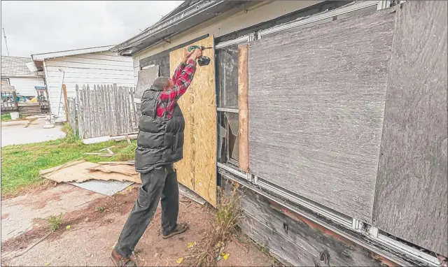  ?? | JIM KARCZEWSKI ?? Christophe­r Jones attaches chipboard to the garage of a house in the 1800 block of 19th Street in Gary where a body was found in October.