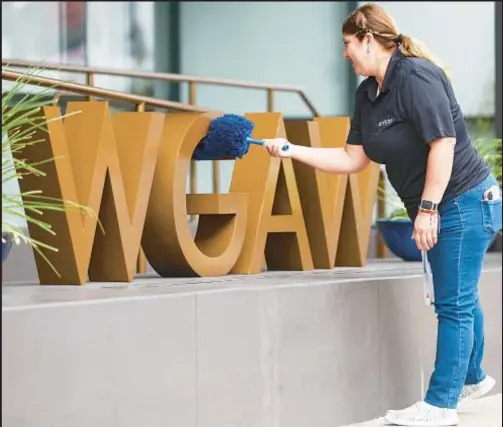  ?? ?? A worker cleans logo displayed outside Writers Guild of America West headquarte­rs on Monday in Los Angeles