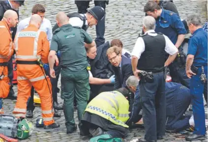  ?? Stefan Rousseau, PA via The Associated Press ?? Conservati­ve Party lawmaker Tobias Ellwood, center, helps perform first aid on a police officer who later died in the attack. The assailant’s body lay about 10 yards away. Journalist Quentin Letts said a man in black attacked the police officer before...