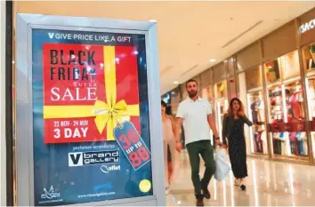  ?? Clint Egbert/Gulf News ?? Customers at a mall in Dubai pass a sign advertisin­g a Black Friday sale by an outlet. Both online and physical stores are running their year-end super sales.