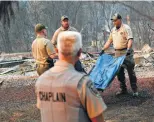  ?? John Locher / Associated Press ?? Deputy Coroner Justin Sponhaltz, right, of the Mariposa County Sheriff ’s Office carries a bag with human remains found at a home burned by the Camp Fire.