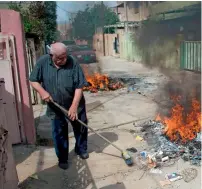  ?? —AFP ?? An Iraqi sweeps old pieces of furniture and garbage into a fire outside his house in Qaraqosh .