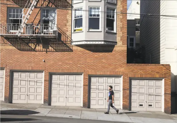  ?? Jessica Christian / The Chronicle ?? Haight-Ashbury Neighbors for Density founder and organizer Phillip Kobernick passes a row of garages as he walks toward his home in the neighborho­od.