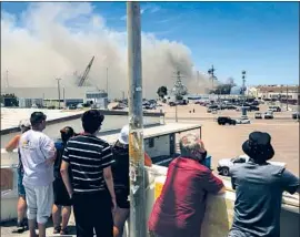  ?? Sam Hodgson San Diego Union-Tribune ?? PASSERSBY watch Sunday as emergency crews respond. Nearly 60 sailors and civilians have been treated for minor injuries related to the firefighti­ng effort.