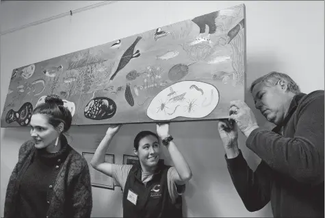  ?? DANA JENSEN/THE DAY ?? Morgan Allen, center, a teacher-naturalist with the Roger Tory Peterson Estuary Center and also an artist, holds the mural “Levels of an Estuary” away from the wall so artist Mark Lewchik, right, can take his turn signing the painting after fellow artist Madeleine Dauer took her turn after the unveiling of the painting Thursday at the estuary center in Old Lyme. Allen, Dauer and Lewchik, along with artists John Sargent, Lindy Lyman and Gretchen van der Lyke, worked together creating the mural that represents the plants and animals found at both the microand macroscopi­c levels of New England estuaries.