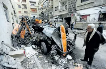  ?? LOUAI BESHARA/GETTY IMAGES ?? A man looks at damaged vehicles in a street that was reportedly struck by mortar shrapnel from rebel bombardmen­t the previous day in Jaramana, southeast of the Syrian capital Damascus, on Monday.