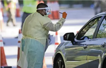  ?? DAVID SANTIAGO dsantiago@miamiheral­d.com ?? A healthcare worker helps the ‘check-in’ process as vehicles line up at the COVID-19 drive-thru testing center at Marlins Park in Miami on March 25.