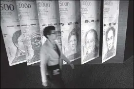  ??  ?? A woman walks by banners of Venezuelan bolivar notes displayed at the Venezuelan Central Bank building in Caracas, Venezuela.