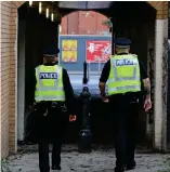  ??  ?? A police officer walks through an area used by drug users. The ground is covered in used drug parapherna­lia (needles, spoons etc) lying abandoned by drug users in an area of land adjacent to London Road,