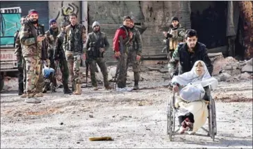  ?? GEORGE OURFALIAN/AFP ?? A member of the Syrian government’s forces pushes an injured woman in a wheelchair as civilians are evacuated from Aleppo’s al-Shaar neighbourh­ood on Wednesday.