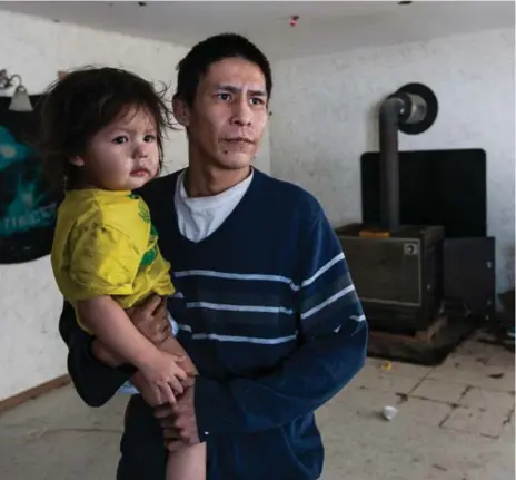  ?? JESSE WINTER/TORONTO STAR ?? Donald Spade holds son Minaateh inside their house in Mishkeegog­amang First Nation in northern Ontario. The house has only a wood stove for heat.