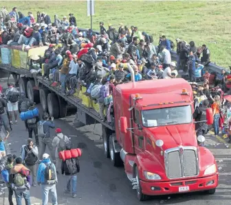  ?? AP ?? HITCHING A RIDE: Central American migrants, above, get a ride on an 18-wheeler pulling a trailer, in Irapuato, Mexico, yesterday on their way to the U.S. border. Below, migrants get settled yesterday at Benito Juarez Auditorium, which is being used as a shelter, in Guadalajar­a, 1,550 miles from the border town of Tijuana.