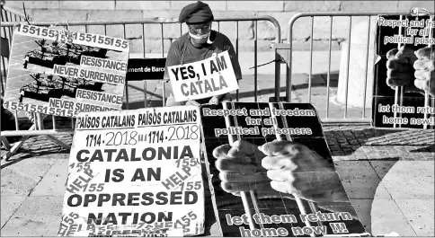  ??  ?? A man wearing a barretina Catalan hat and with his mouth covered with a white cloth, holds a placard reading ‘Yes, i am Catalan’ in front of the Generalita­t Palace in Barcelona.