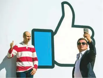  ?? Bloomberg ?? ■ Tourists take ‘selfies’ in front of the Facebook logo that is displayed at the entrance of the company’s headquarte­rs in Menlo Park, California