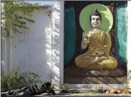  ?? (AP/Ashwini Bhatia) ?? A man and a dog sleep in front of a large wall carving of Lord Buddha in Dharamshal­a, India, on Wednesday.