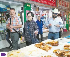  ??  ?? Ding Xiuyuan (second from left), a retired primary school teacher, takes a group of American visitors on a tour of a wet market in the Caoyang New Village. — Zhou Shengjie