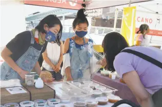  ?? Paul Chinn / The Chronicle ?? Mariko Grady ( left) and Kana Weaver help a customer at Grady’s Aedan Fermented Foods stand at the Ferry Plaza Farmers Market in S. F. Grady says some of her favorite farmers’ market vendors lost their farms in fires near Santa Cruz.