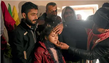  ?? AP ?? Malak Saad Dakhel, 11, is anointed by a holy man inside a Yazidi shrine in February this year as she is welcomed home in Sharia, Iraq, by her relatives after her escape from Syria. She was captured by Islamic State militants in 2014 and was recently found at al-Hol camp living with a Syrian family.