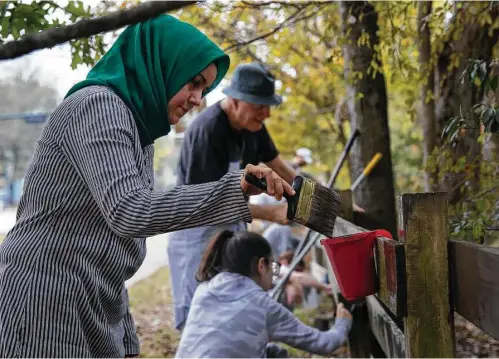  ?? Annie Mulligan ?? Huriye Ercetin and fellow volunteers paint the fence surroundin­g Bellaire’s Nature Discovery Center during an interfaith community service project.