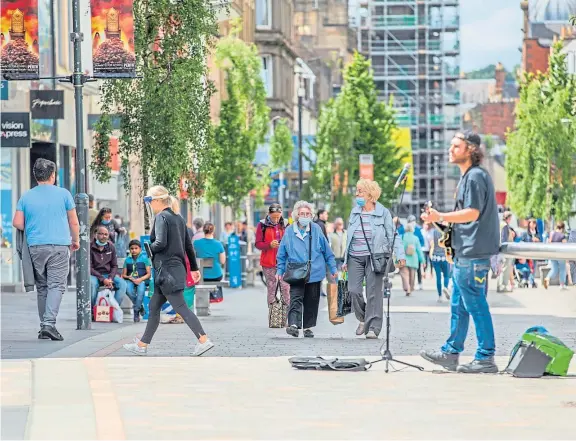  ??  ?? Street life: A busker performs as shoppers pass by – many wearing masks – as the ‘new normal’ sets in on Perth High Street.