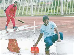  ?? (Pics: Ntokozo Magongo) ?? Athletics Official Micite Thusi (L) and Manzini Athletics Coach (MAC) Muzi Mabuza attempt to clear the water on the track after the rain on Saturday.