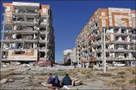  ?? OMID SALEHI / ASSOCIATED PRESS ?? Survivors sit near damaged buildings Monday in Sarpol-e-Zahab, in western Iran, the day after Sunday night’s earthquake. Outside walls of some apartment complexes were sheared off and power and water lines were severed.