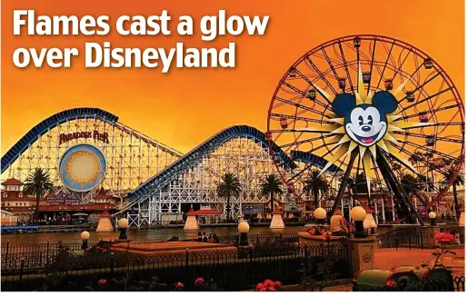  ??  ?? Eerie: Light from the blaze in the Anaheim Hills creates an orange shadow over the rides at the Disneyland resort