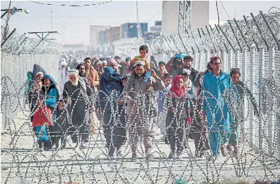  ?? AFP VIA GETTY IMAGES ?? Afghans walk along fences as they arrive in Pakistan through the Pakistan-Afghanista­n border crossing point Tuesday. According to the United Nations, 250,000 Afghans have fled their homes since the U.S. troop withdrawal and fighting with the Taliban began.