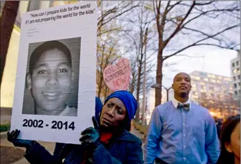  ??  ?? In this Dec. 1, 2014, file photo, Tomiko Shine (left) holds a sign with a photo of Tamir Rice, a boy fatally shot by a Cleveland police officer, while protesting a grand jury’s decision in Ferguson, Mo., not to indict police officer Darren Wilson in...