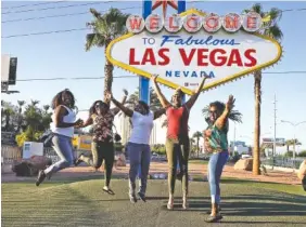  ?? THE ASSOCIATED PRESS ?? Tourists pose for photos Tuesday in front of the Welcome to Las Vegas sign, where people left flowers honoring vicrtims of Sunday’s mass shooting in Las Vegas.