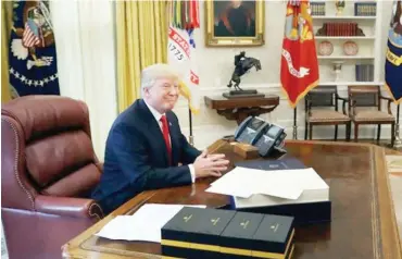 ??  ?? Mr Trump sits at the White House Resolute Desk in the Oval Office