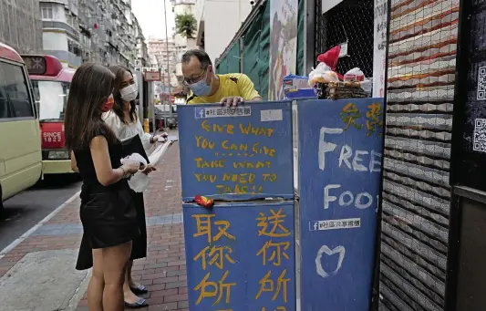  ?? VINCENT YU AP ?? Two women chat with Ahmed Khan, right, after putting foods inside the refrigerat­or at Woosung Street in Hong Kong. Khan, founder of a sports foundation on the same street, said he was inspired to create a community refrigerat­or after seeing a film about others doing the same thing.