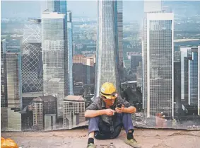  ?? Andy Wong, The Associated Press file ?? A worker browses his smartphone outside a constructi­on site wall depicting the skyscraper­s in the Chinese capital at the Central Business District in Beijing. After galloping along for the past two years, the global economy is showing signs of weakening, with the United States, China and Europe all facing the rising threat of a slowdown.