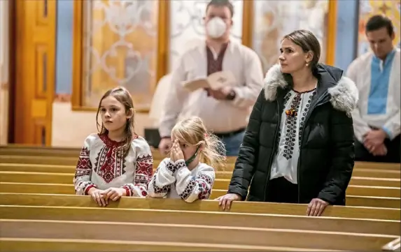  ?? Alexandra Wimley/Post-Gazette photos ?? Victoria, 9, Sophia, 5, and their mother Oksana Kukhar, of Scott, pray during a service for peace in Ukraine on Wednesday at Holy Trinity Ukrainian Catholic Church in Carnegie. Some congregant­s wore traditiona­l Ukrainian embroidery to show solidarity to those in Ukraine.