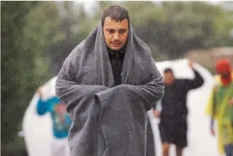  ??  ?? Syrian refugees walk through rain and fog on their way to the nearest registrati­on camp on the island of Lesvos, Thursday.