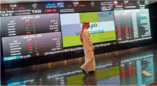  ?? — AFP ?? An investor walking past stock exchange monitors at the Saudi Stock Exchange in Riyadh.
